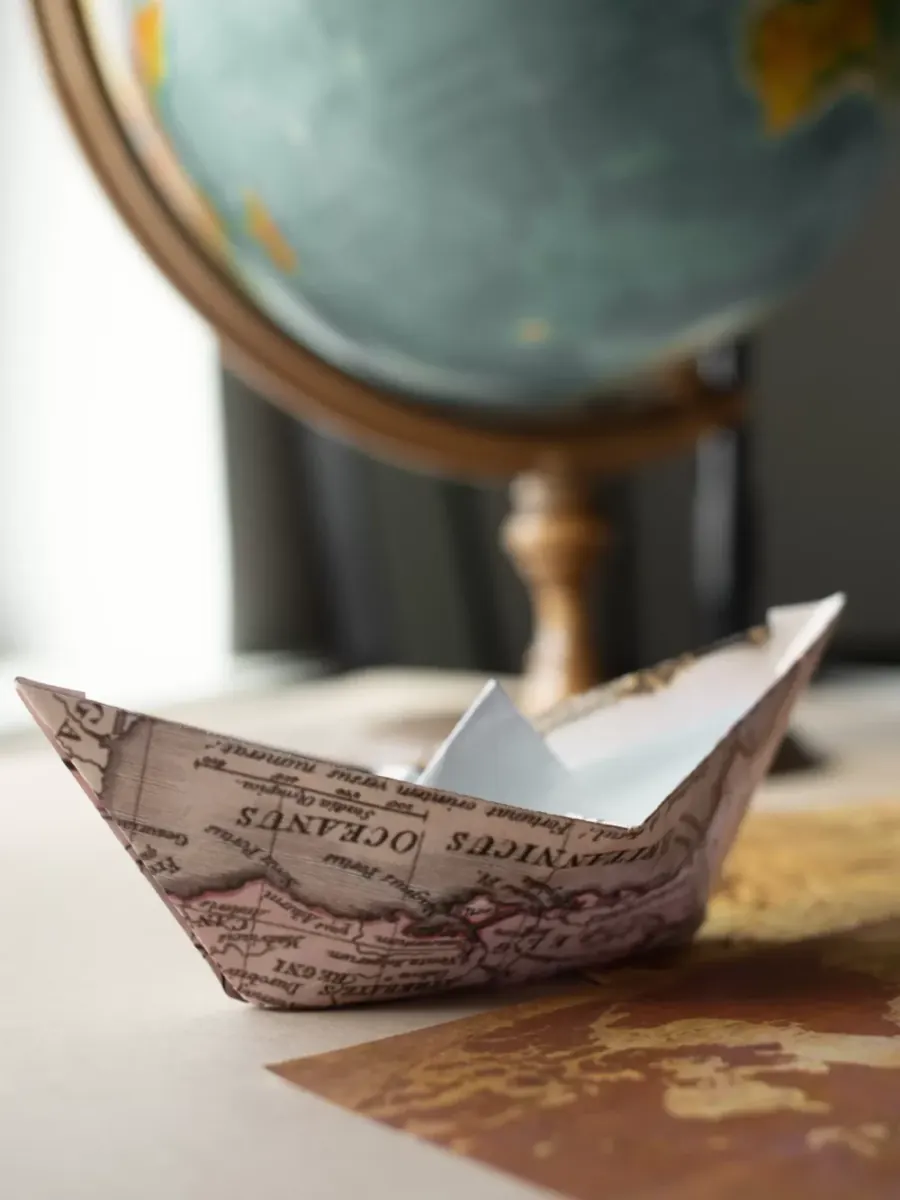 Paper boat on a map next to a globe